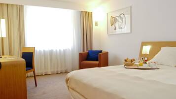 A hotel room with a bed, a desk with a chair, a window with curtains, and a breakfast tray on the bed.