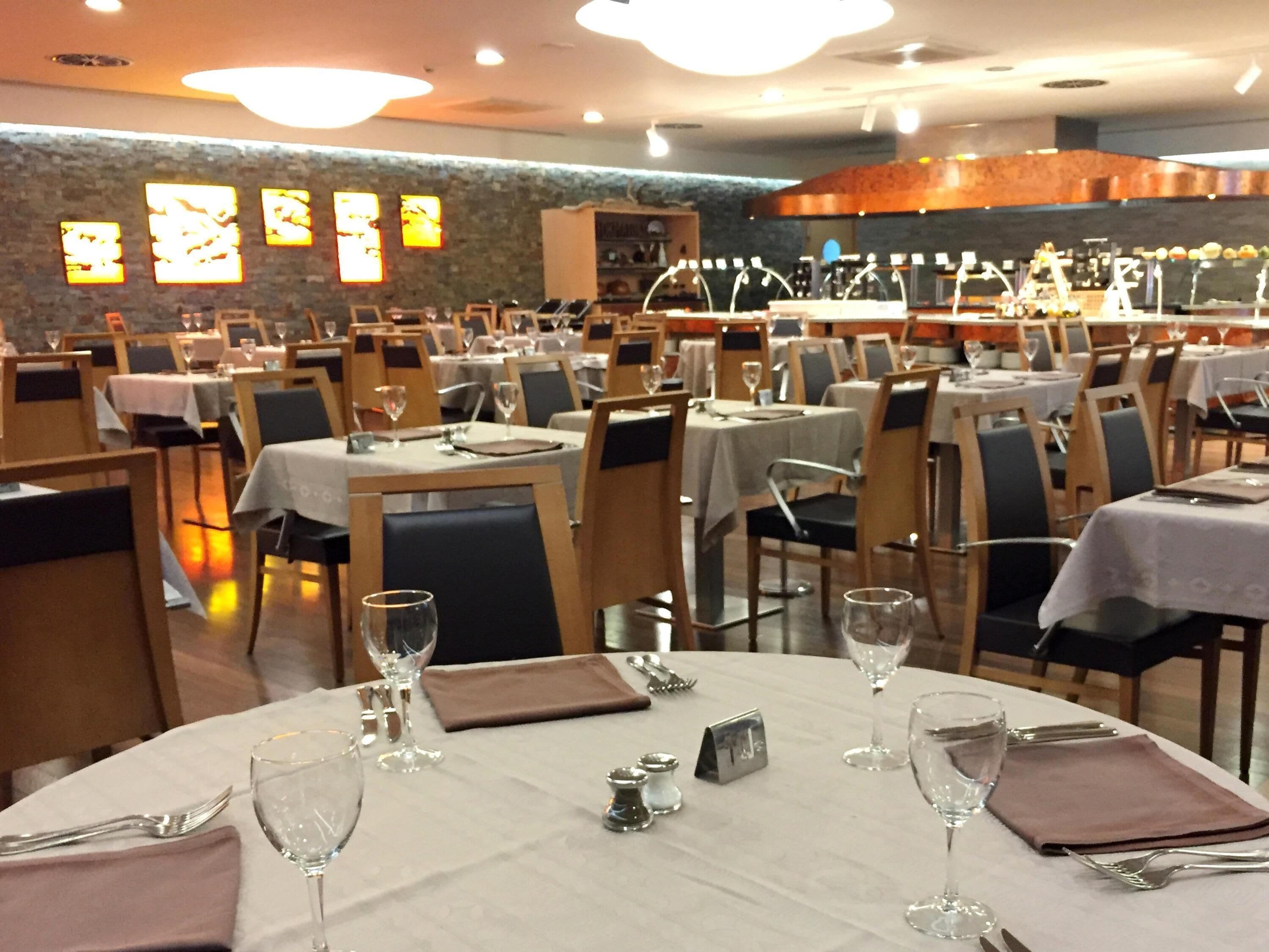 Un restaurante con mesas redondas, sillas y una pared de piedra con letreros iluminados.