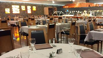 Un restaurante con mesas redondas, sillas y una pared de piedra con letreros iluminados.