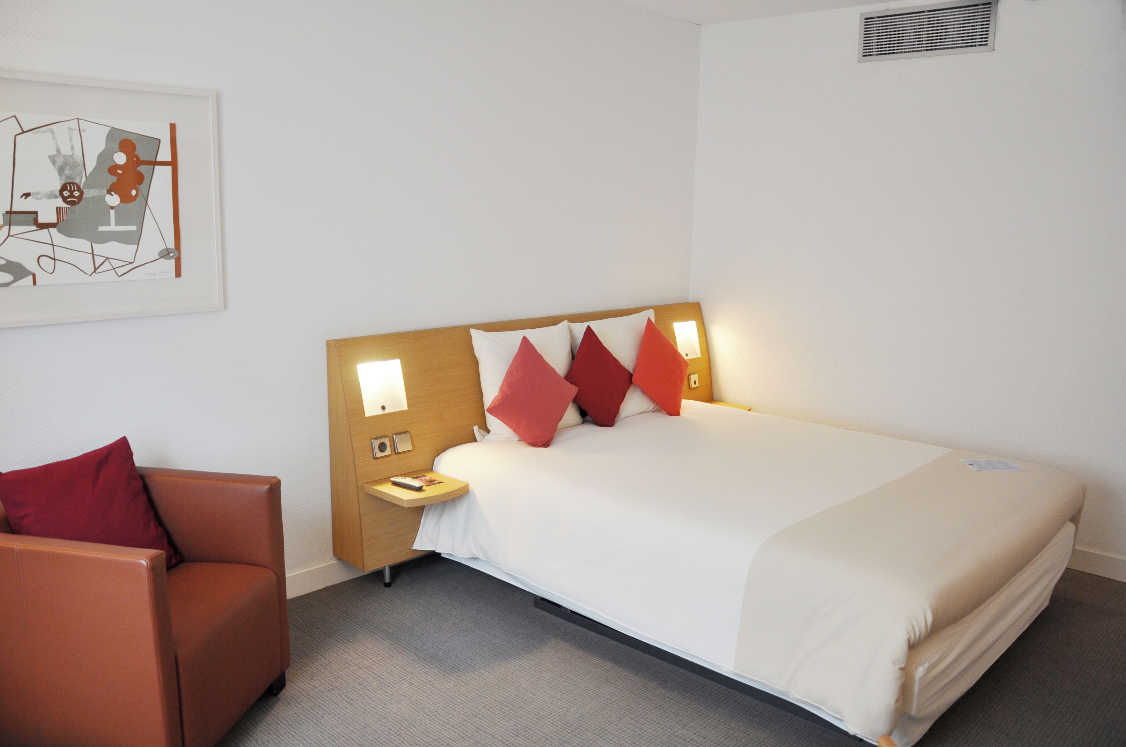 Una habitación de hotel con una cama, una mesita de noche, una silla y una obra de arte colgada en la pared.