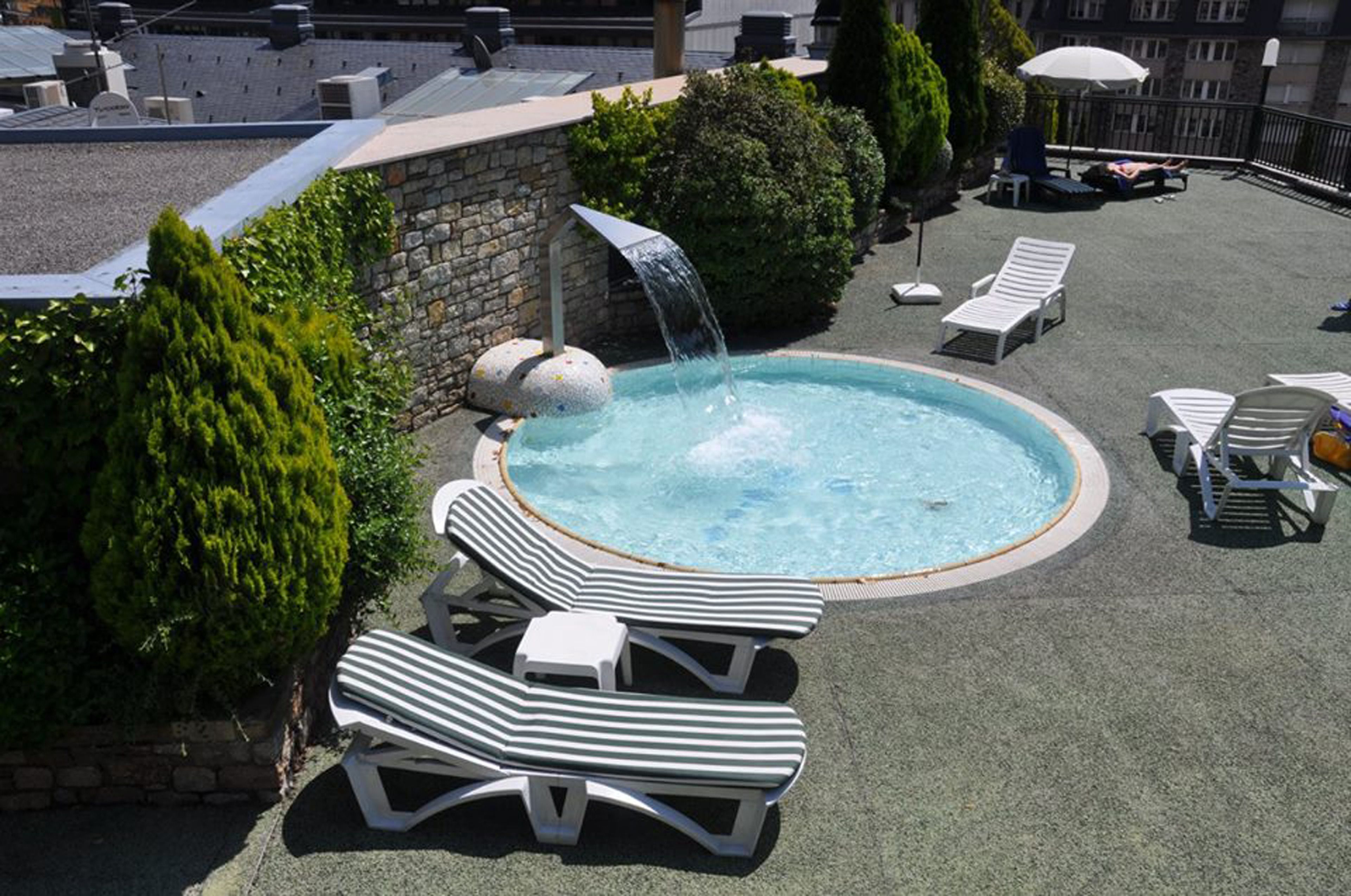A rooftop pool with a waterfall feature, surrounded by lounge chairs and a stone wall.