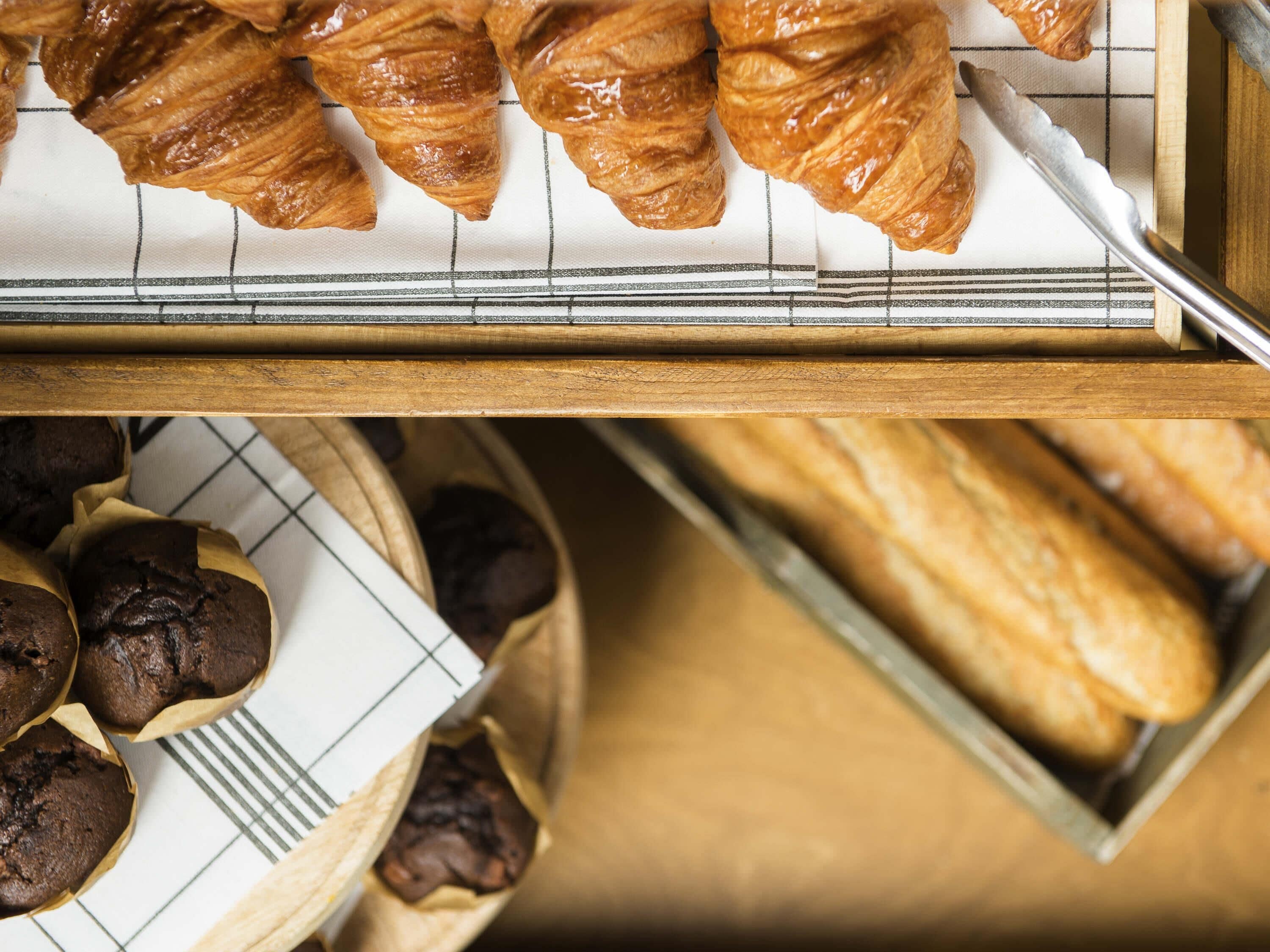 A tray of pastries including croissants and muffins, a knife, and a wooden cutting board.