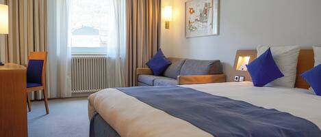 A hotel room with a large bed, a desk, a chair, and a window with curtains.