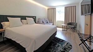 A hotel room with a large bed, a desk, a chair, a TV, and a window with curtains. - Novotel Andorra (Andorra la Vella)
