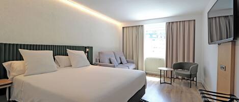 A hotel room with a large bed, a desk, a chair, a TV, and a window with curtains.