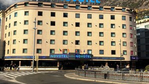 A hotel named Novotel with a curved facade, multiple windows, and a view of mountains in the background. - Novotel Andorra (Andorra la Vella)