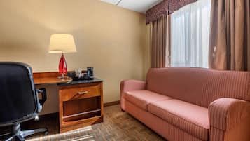 Une chambre d’hôtel avec un bureau en bois, une lampe rouge, un fauteuil de bureau noir et un canapé à rayures.