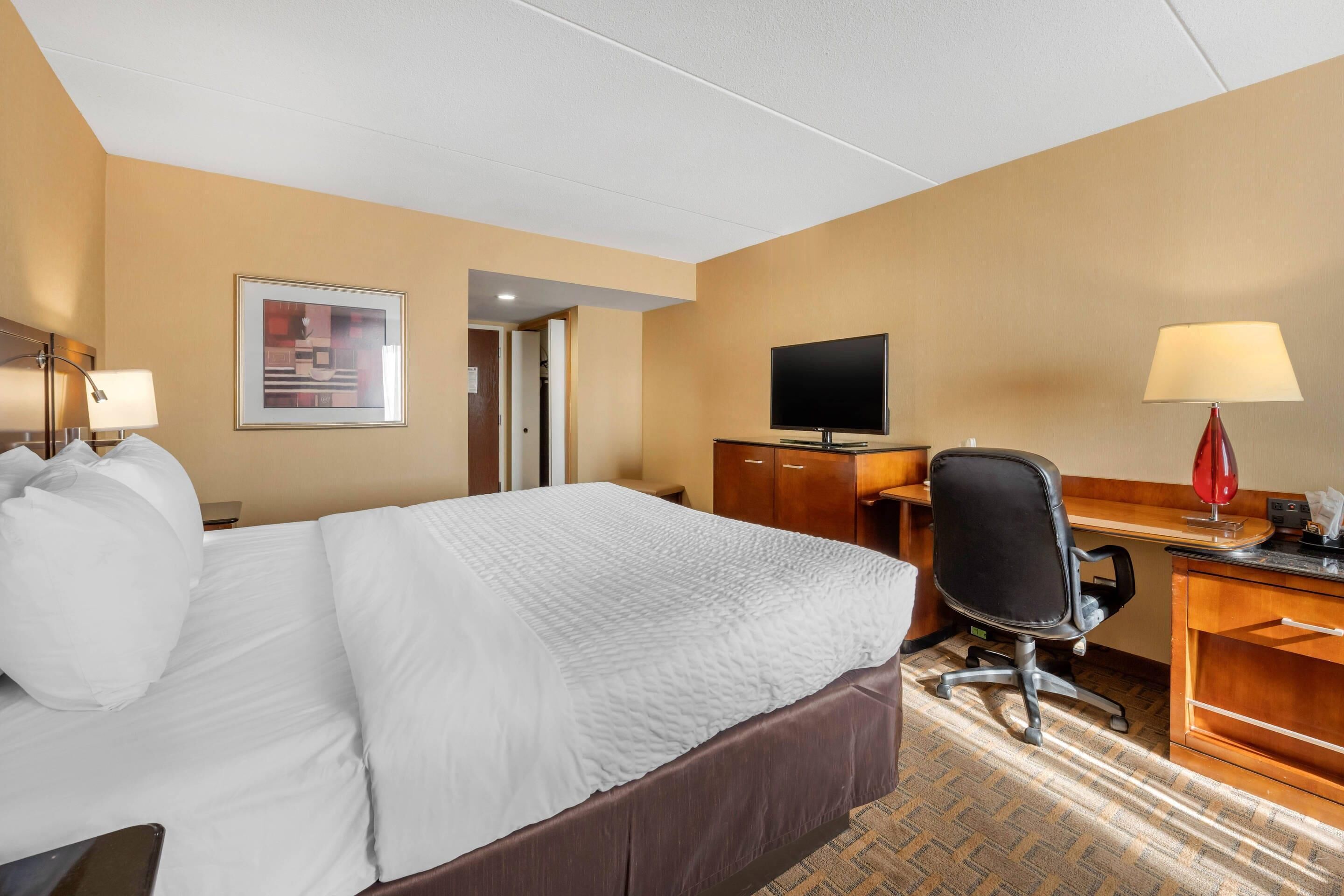 A hotel room with a large bed, a desk with a computer, a TV, and a lamp.