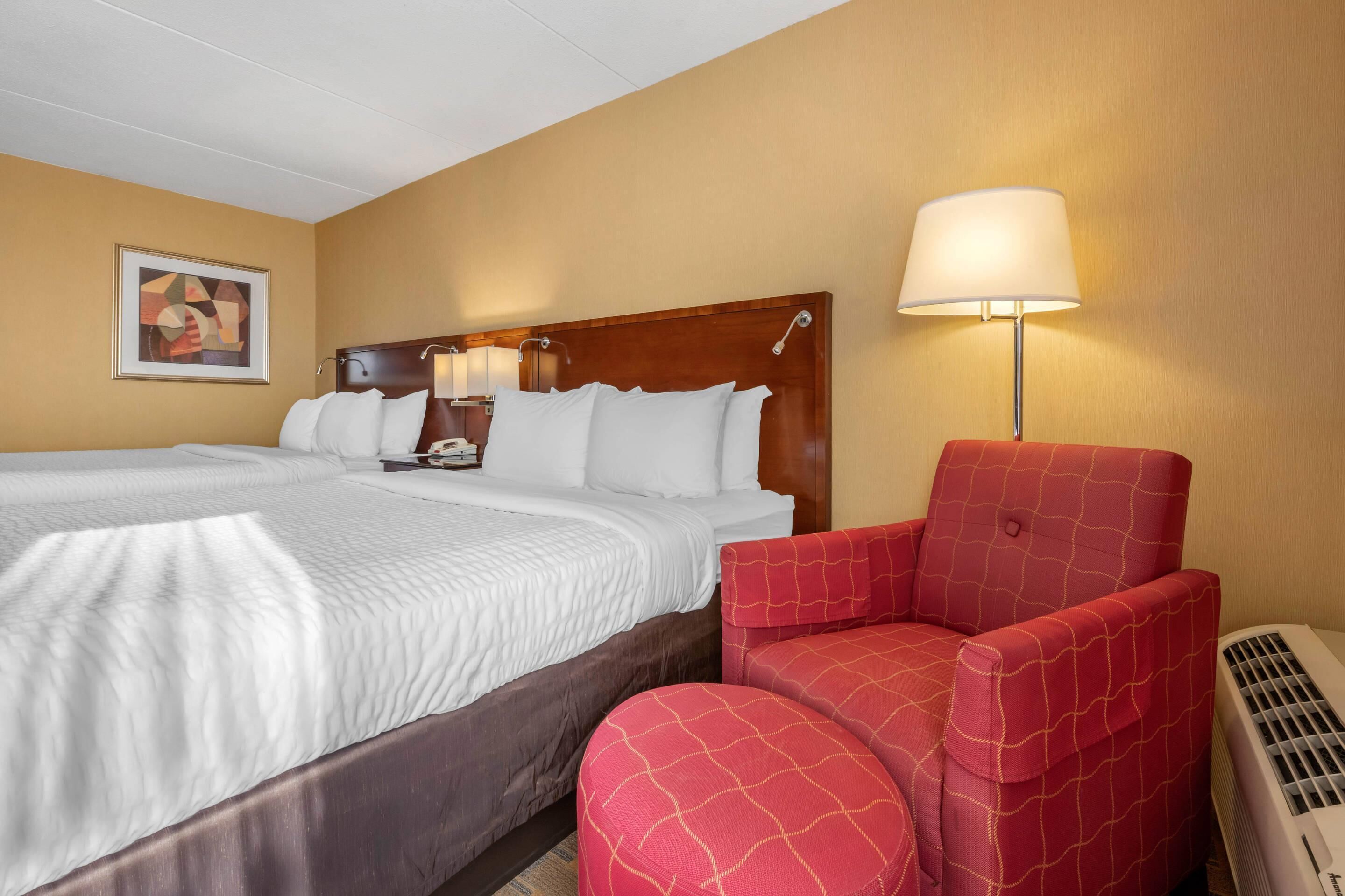 A hotel room with a double bed, a red armchair, a standing lamp, and a framed picture on the wall.