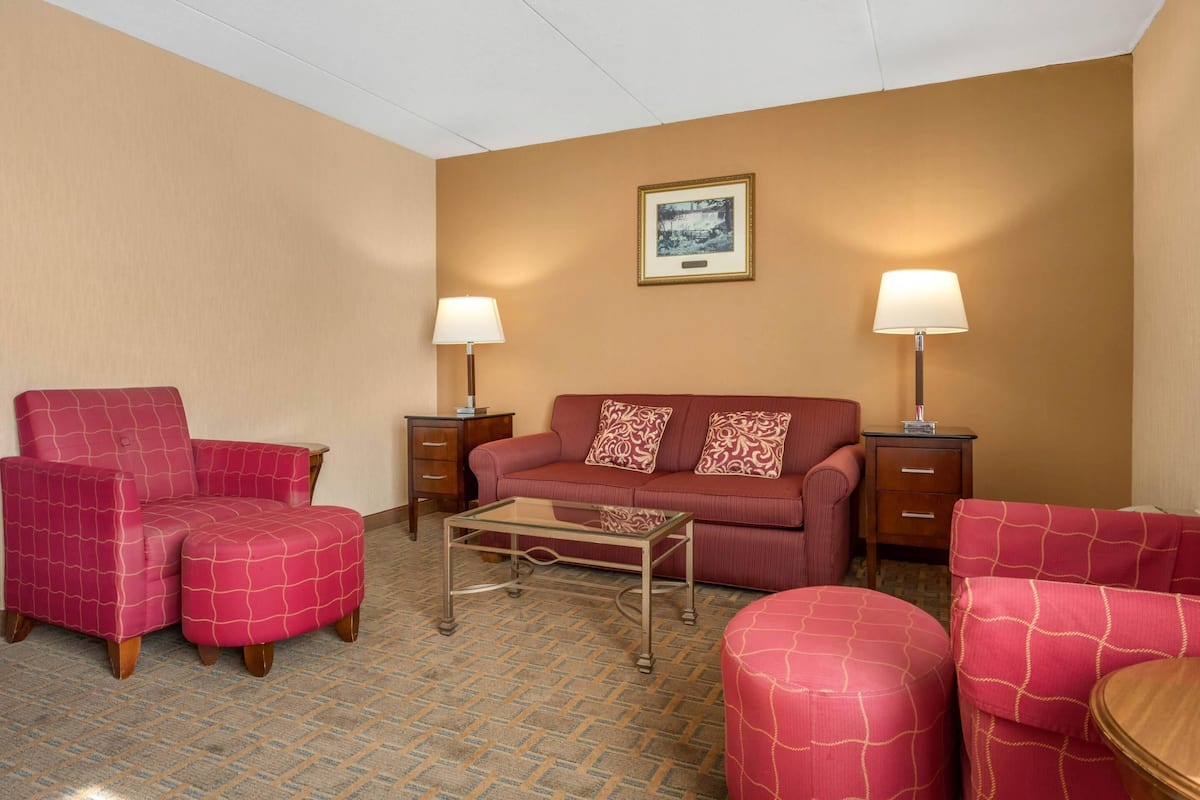 Habitación de hotel con un sofá tapizado rojo, un sillón a juego, una mesa de centro de vidrio y dos mesitas de noche con lámparas.