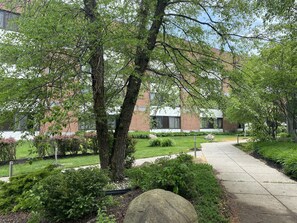 A landscaped courtyard with a pathway, trees, and a building with large windows in the background.