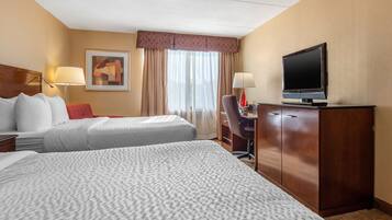 A hotel room with two beds, a desk, a television, and a window with curtains.