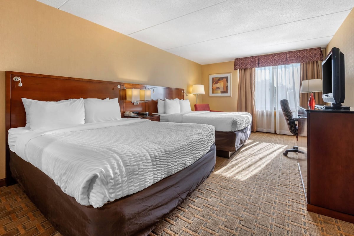 Habitación de hotel con dos camas, un escritorio, una silla, un televisor y una ventana con cortinas.