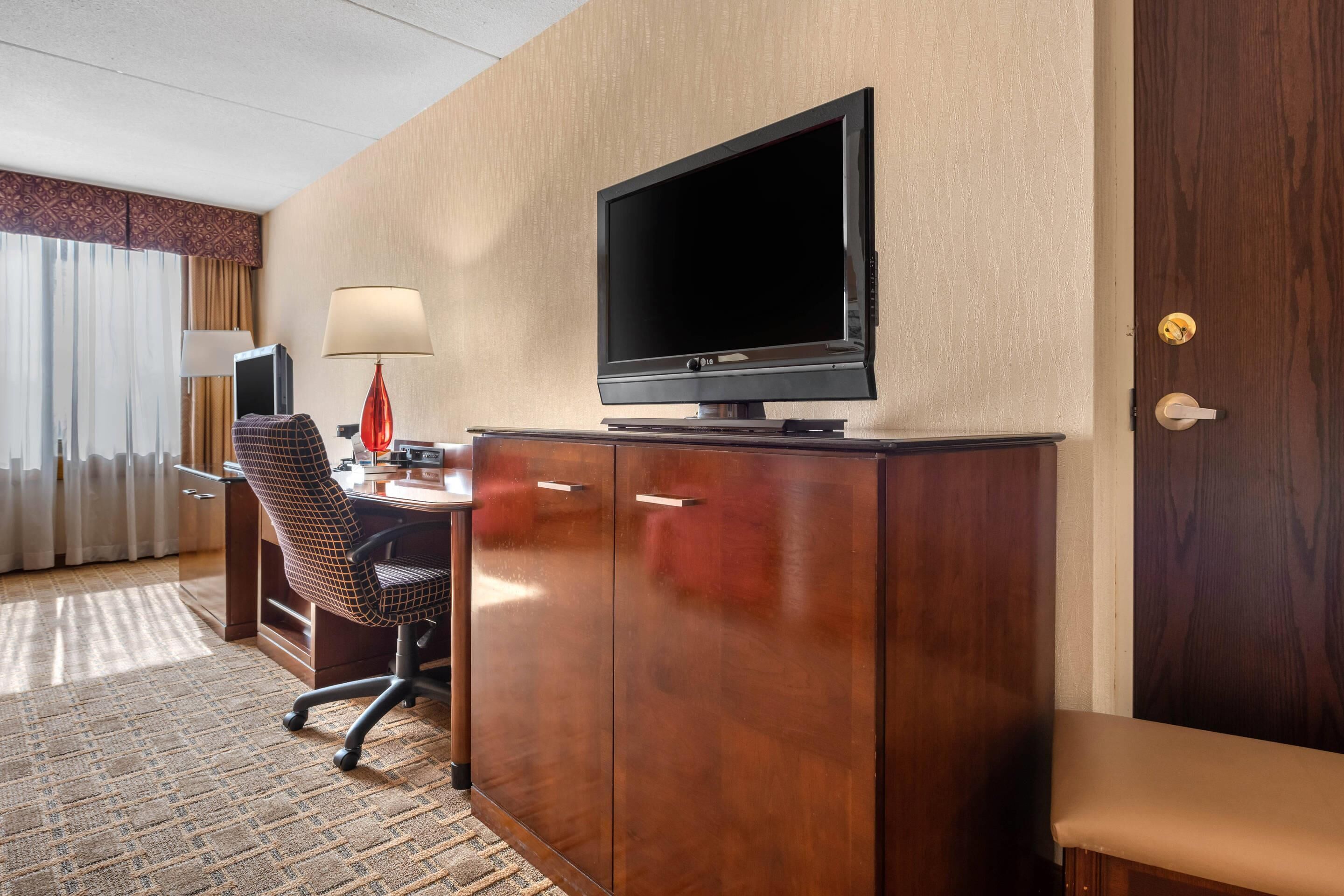 Una habitación de hotel con un escritorio de madera, un televisor, una silla, una lámpara y una cama.