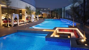 Une piscine dotée d’un espace salon en contrebas, entouré de chaises longues et d’un espace salon couvert avec des coussins rouges.