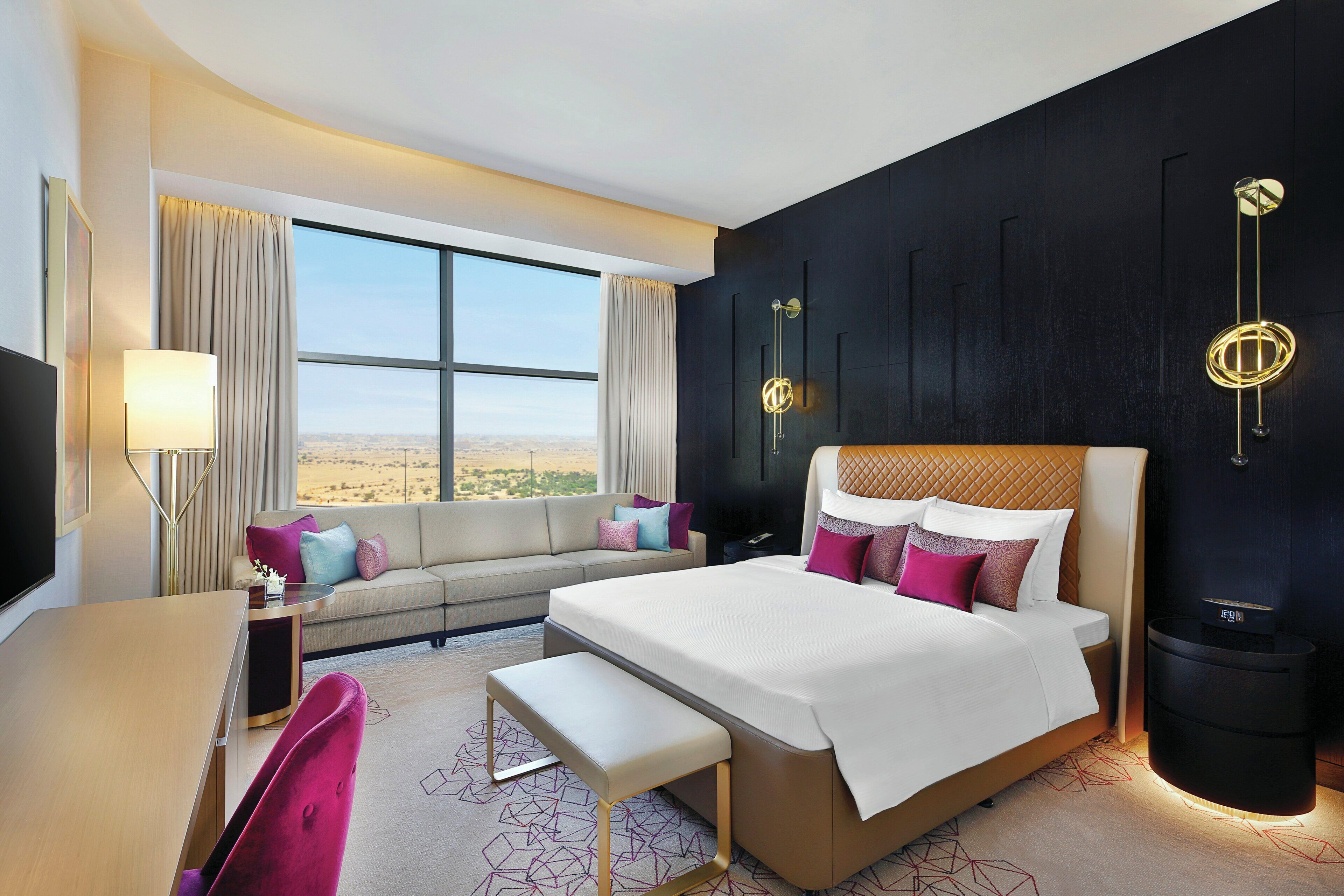 A modern hotel room with a large bed, a sofa, a desk, and a view of the desert.