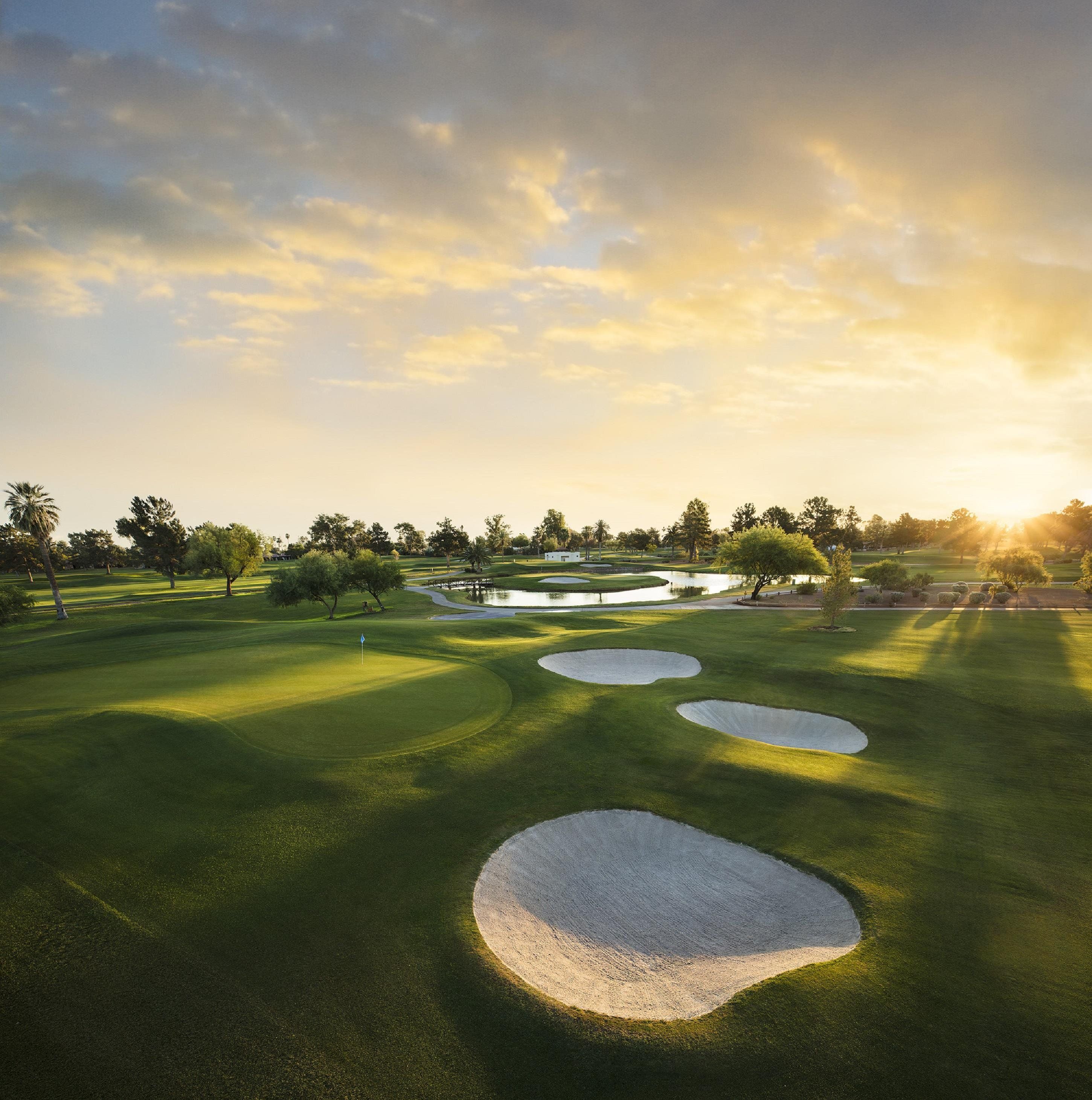 A golf course with sand bunkers, a pond, and trees under a clear sky.