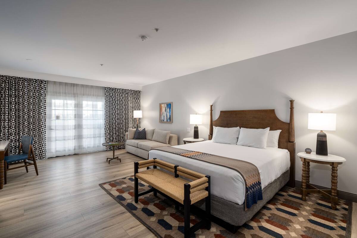 A modern hotel room with a large bed, a sofa, a small table, and a bench.