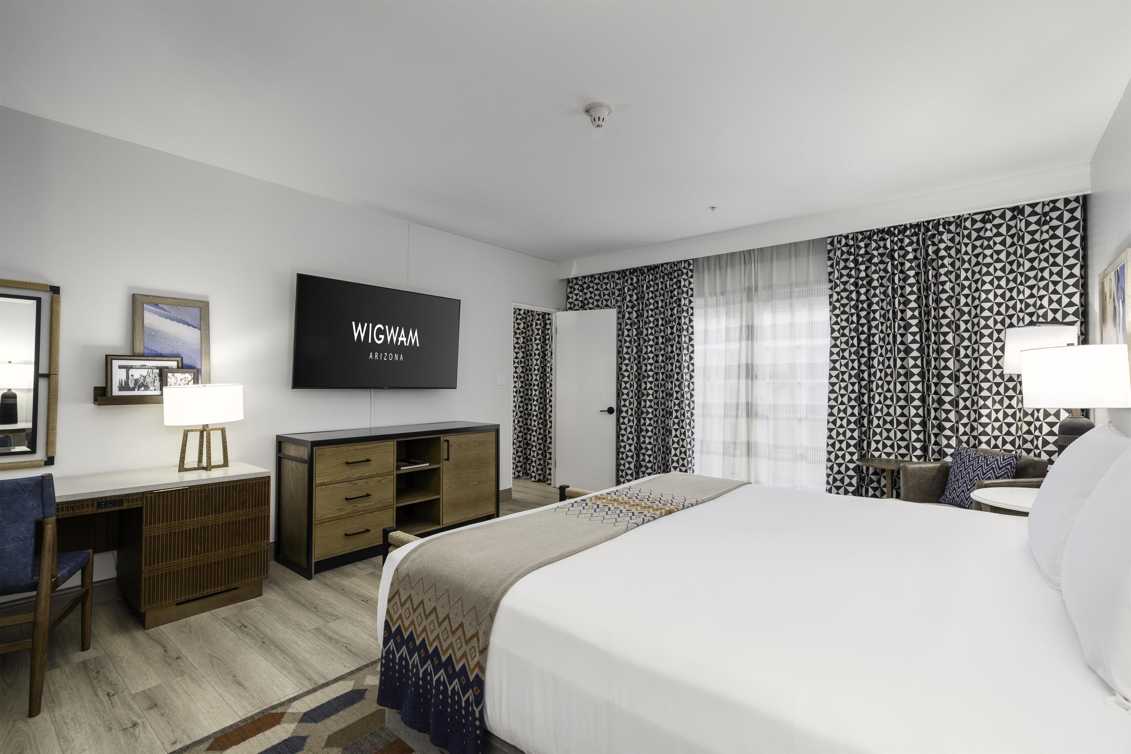 Une chambre d’hôtel avec un lit, un bureau doté d’une lampe, une télévision et un mur orné d’un motif.