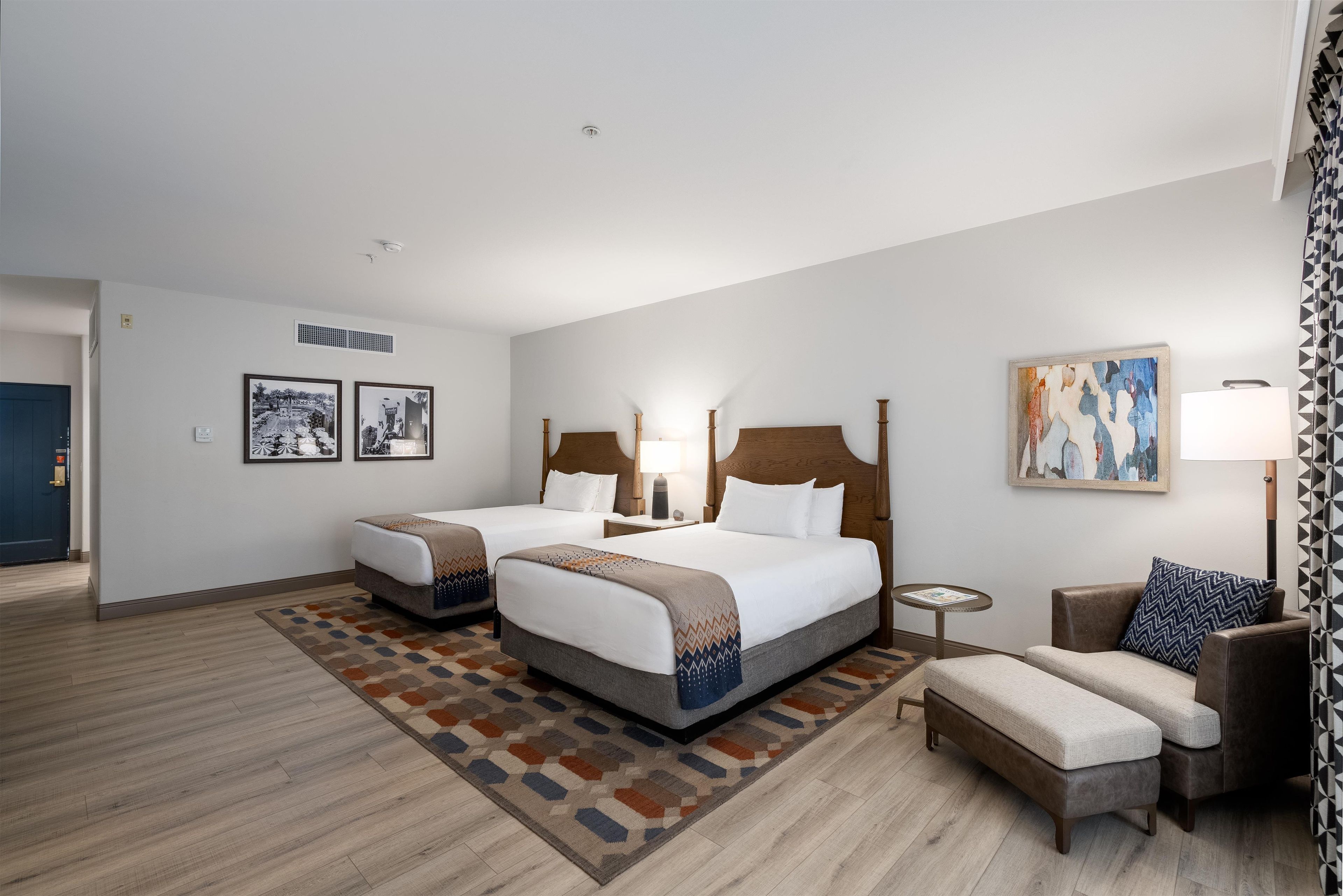 A hotel room with two beds, a sofa, a small table, and artwork on the walls.