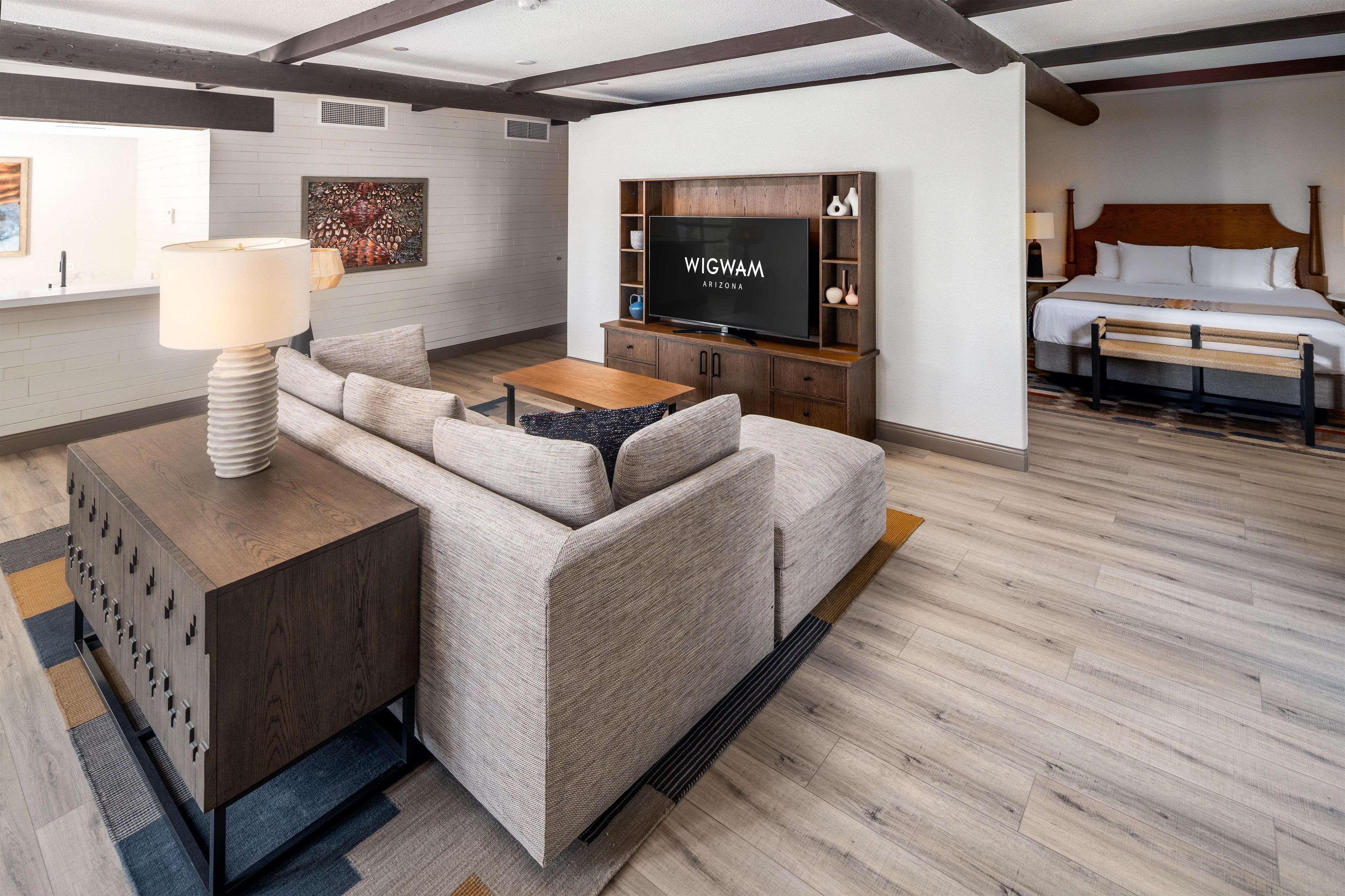 Ett modernt hotellrum med en soffa, ett litet bord i trä, en platt-TV och en säng med ett huvudgavel i trä.