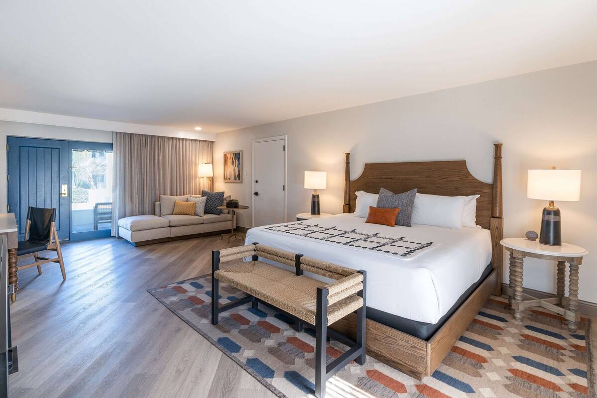 A hotel room with a large bed, a sofa, a bench, and a small table.