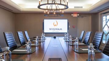 A conference room with a long table, chairs, a projector screen displaying 'WIGWAM ARIZONA', and a chandelier.
