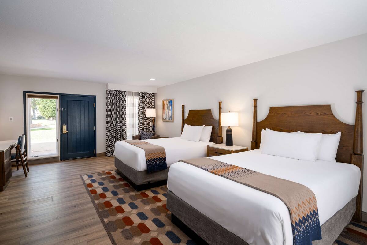 A hotel room with two beds, a desk, and a door leading outside.