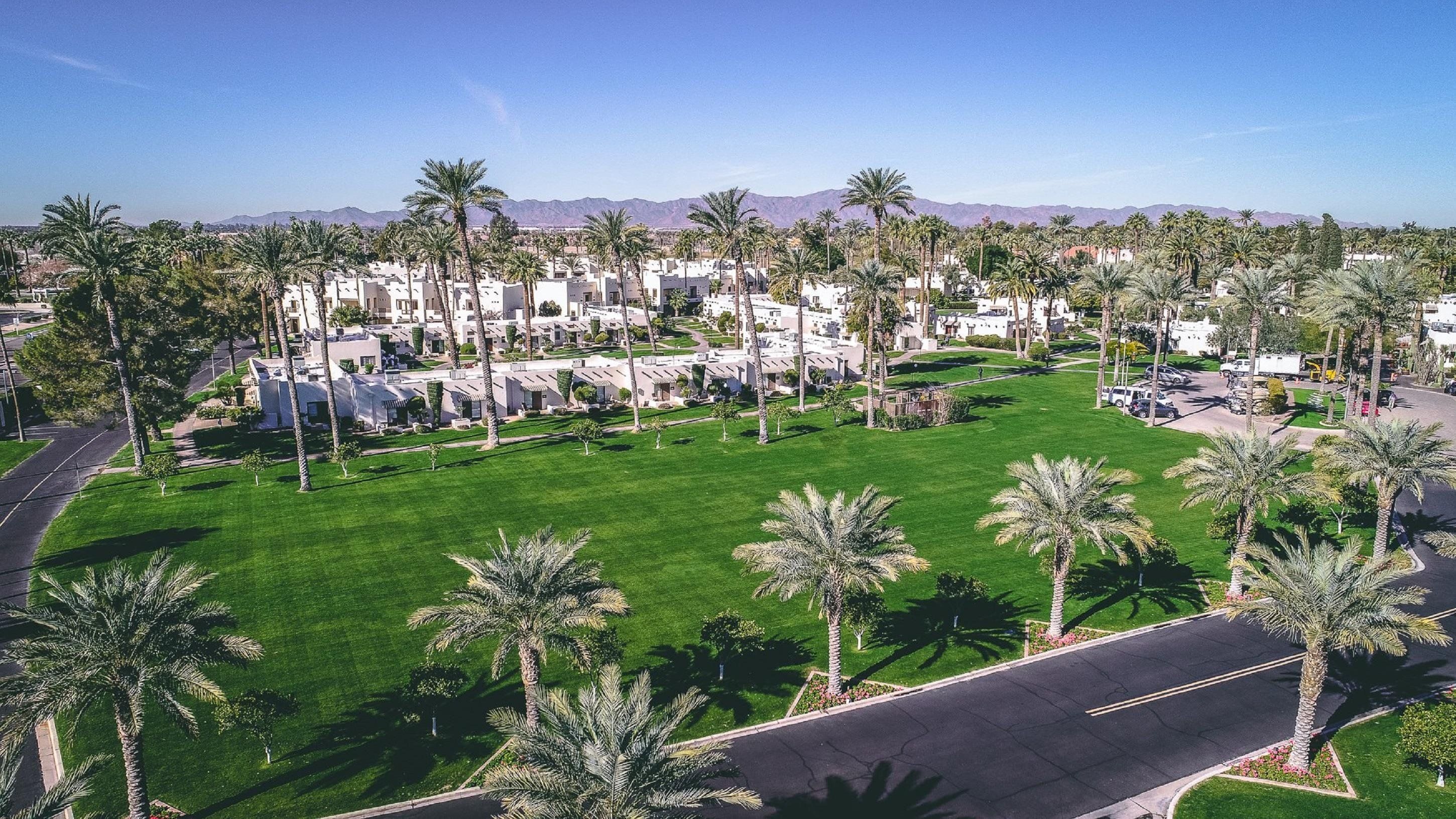 A resort with multiple-story buildings, a well-maintained lawn, and palm trees.