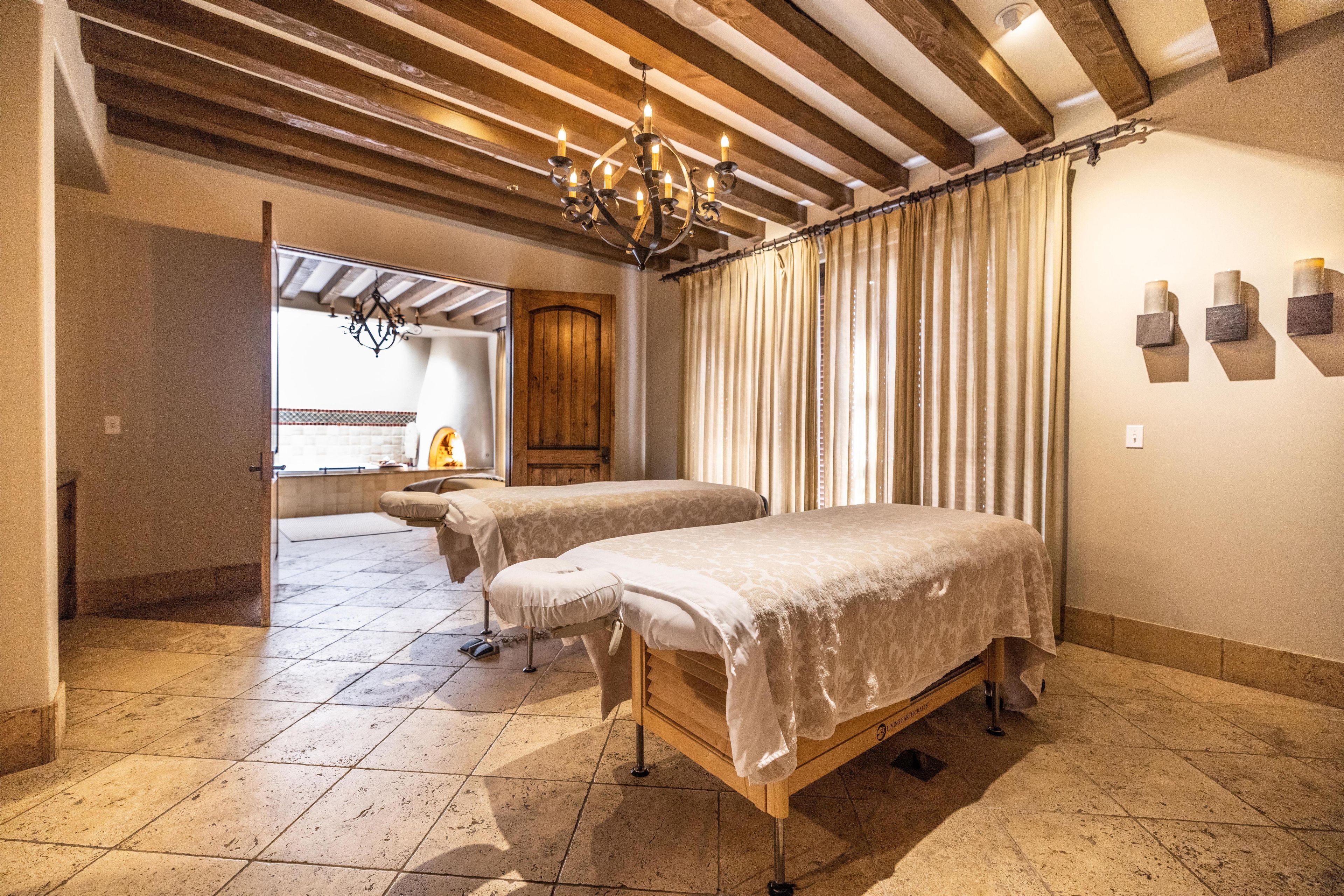 A room with two beds, a wooden ceiling, a chandelier, and a window with curtains.
