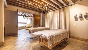A room with two beds, a wooden ceiling, a chandelier, and a window with curtains.