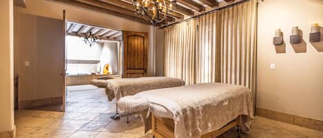 A room with two beds, a wooden ceiling, a chandelier, and a window with curtains.