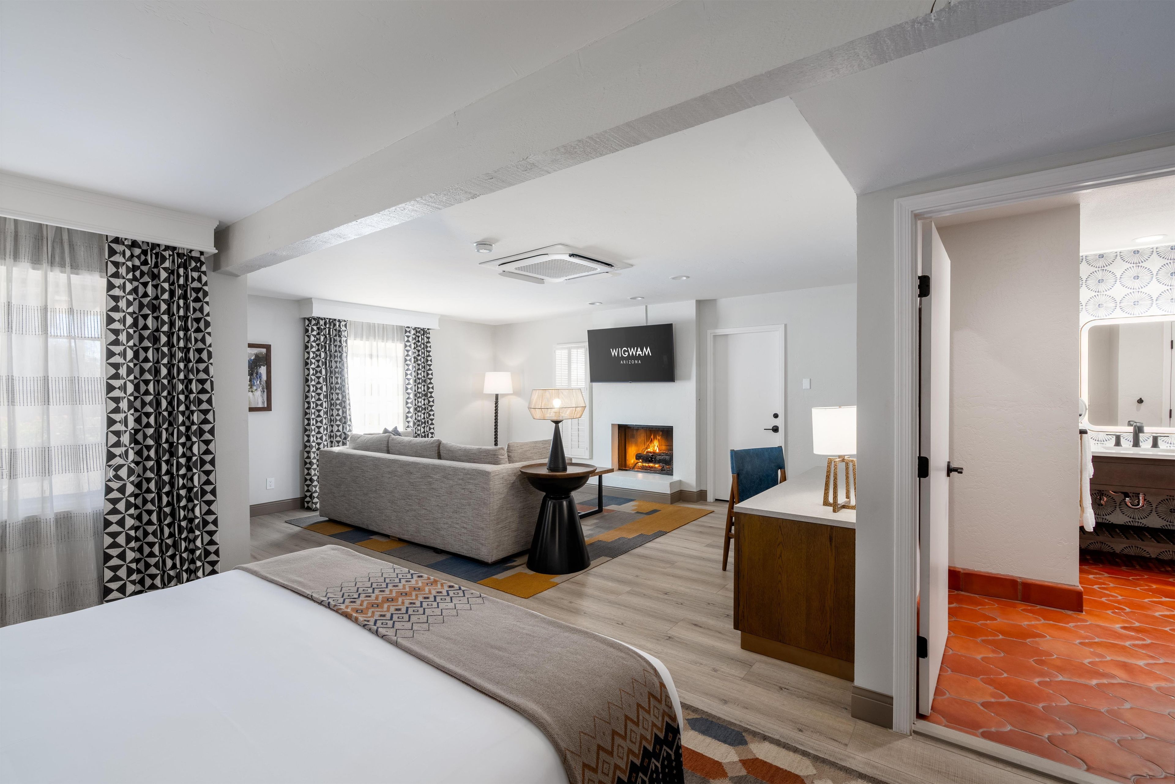 A hotel room with a bed, a sofa, a TV, a fireplace, and a bathroom visible through an open door.