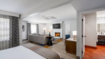 A hotel room with a bed, a sofa, a TV, a fireplace, and a bathroom visible through an open door.