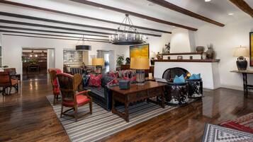 A spacious living room with a fireplace, wooden flooring, and a high ceiling with exposed beams.