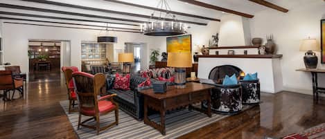 A spacious living room with a fireplace, wooden flooring, and a high ceiling with exposed beams.
