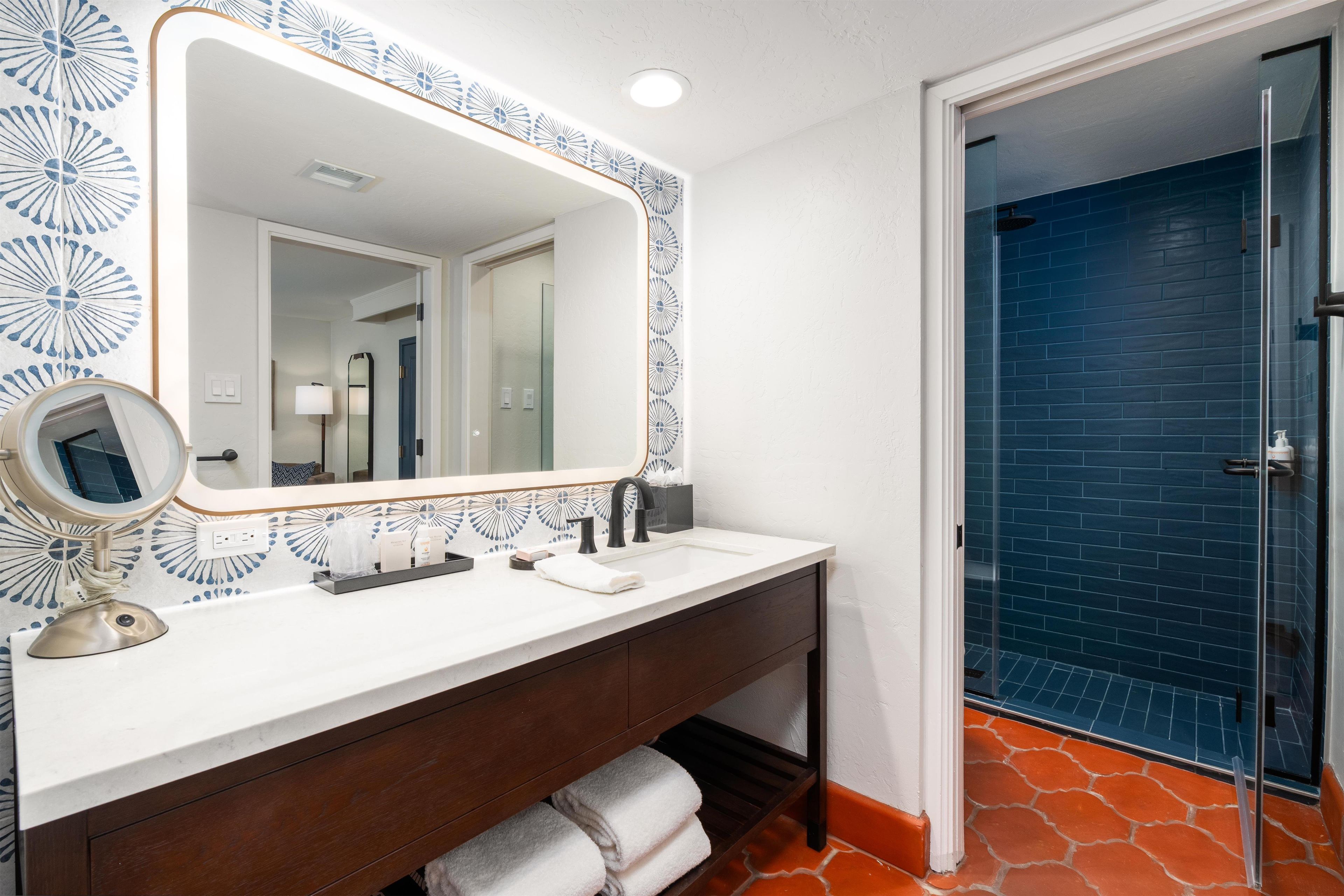 A bathroom with a white vanity, a large mirror, a round mirror, and a blue door.