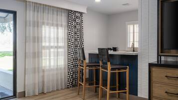 A room with a dining area featuring two bar stools, a kitchen counter, and a large window with blinds.