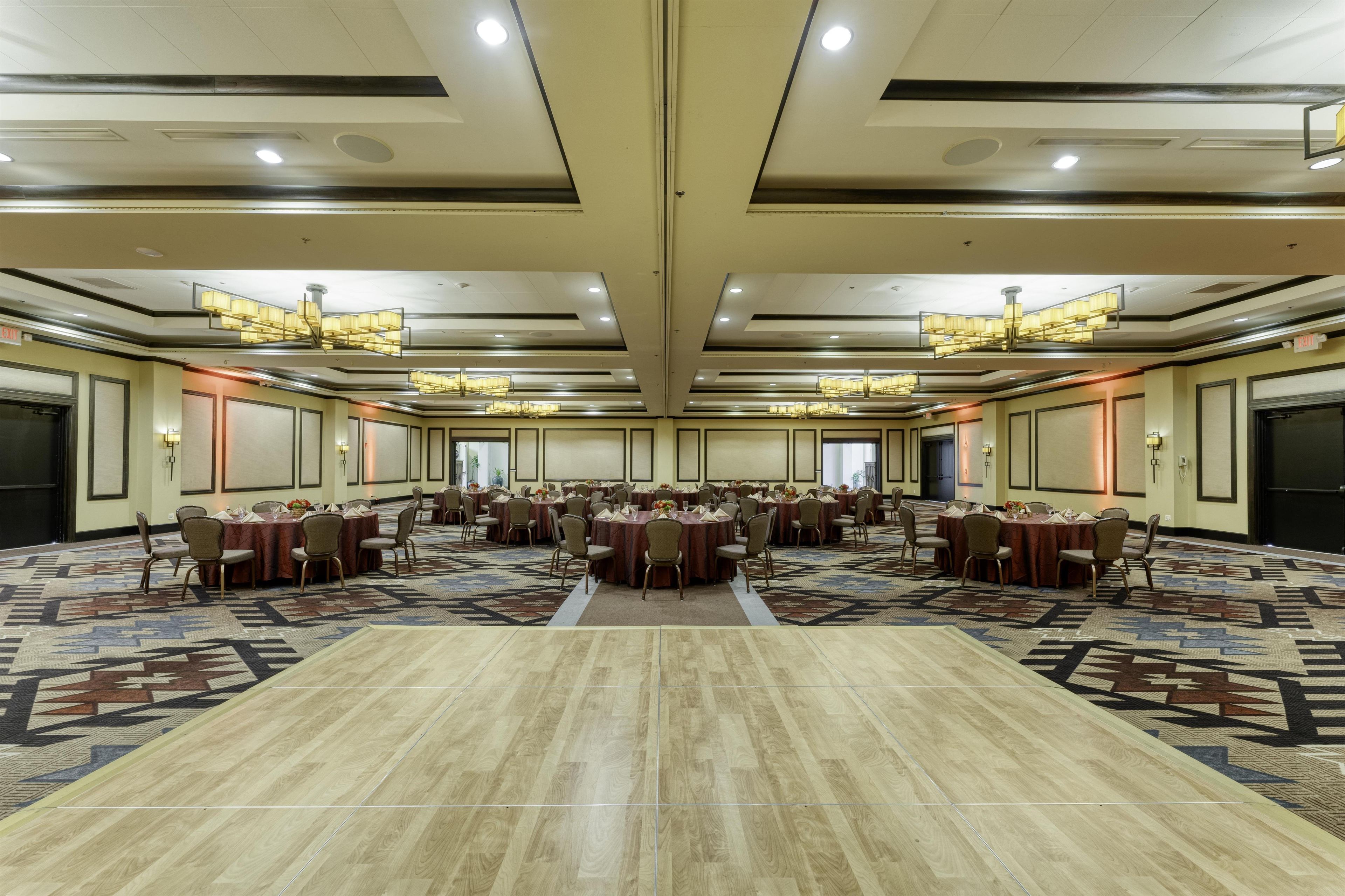 Une grande salle de conférence dotée de nombreuses tables et chaises, d’un tapis à motifs et d’un plafond haut avec des luminaires encastrés.