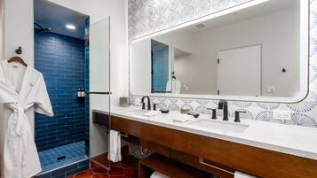 Une salle de bain avec une cabine de douche bleue, une robe blanche suspendue, un grand miroir et un meuble-lavabo en bois doté de deux vasques.