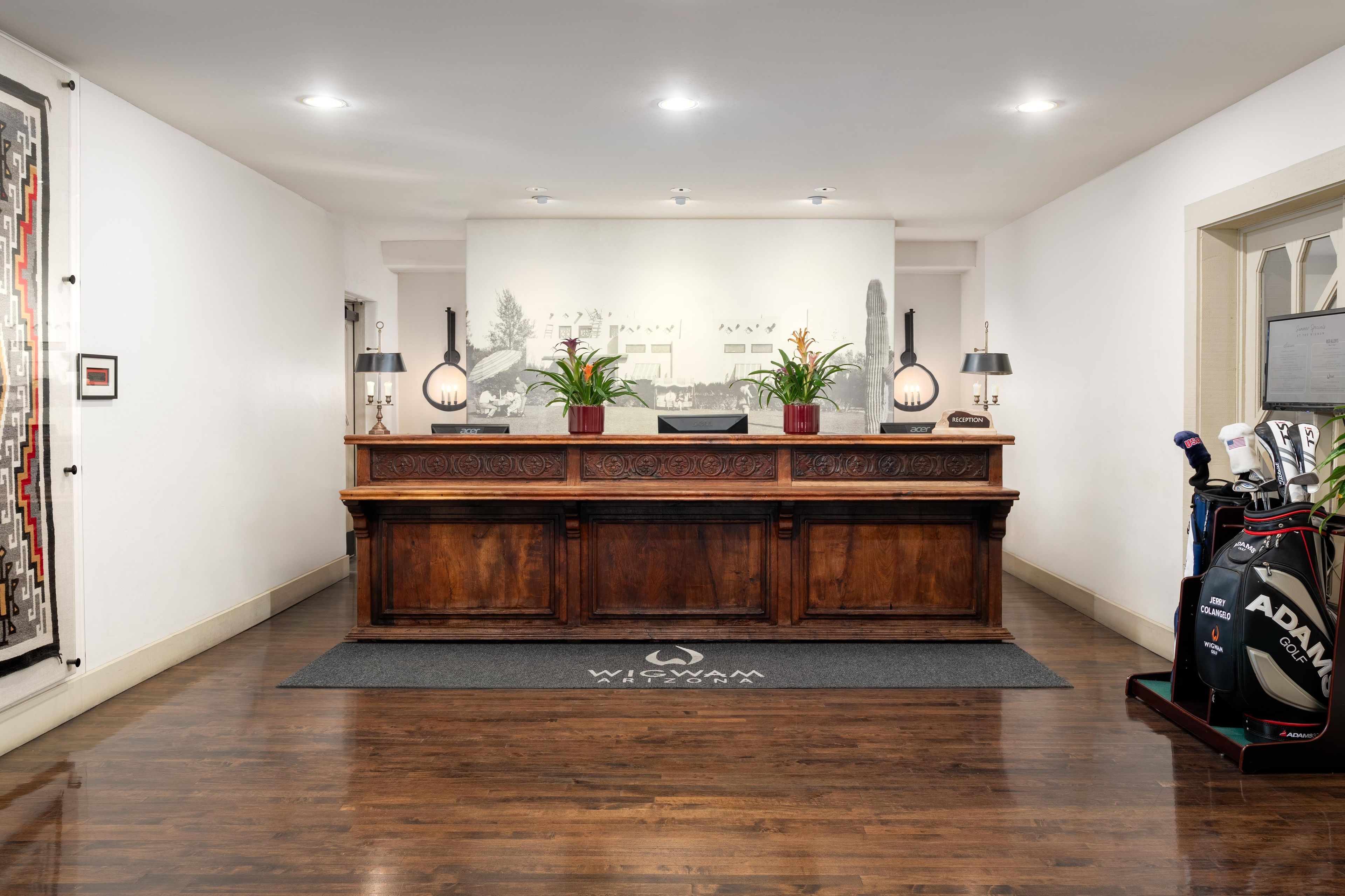 A reception desk with a wooden finish, two potted plants, and a framed welcome sign.