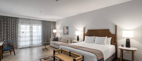 A hotel room with a large bed, two bedside tables, a sofa, a chair, and a small table.