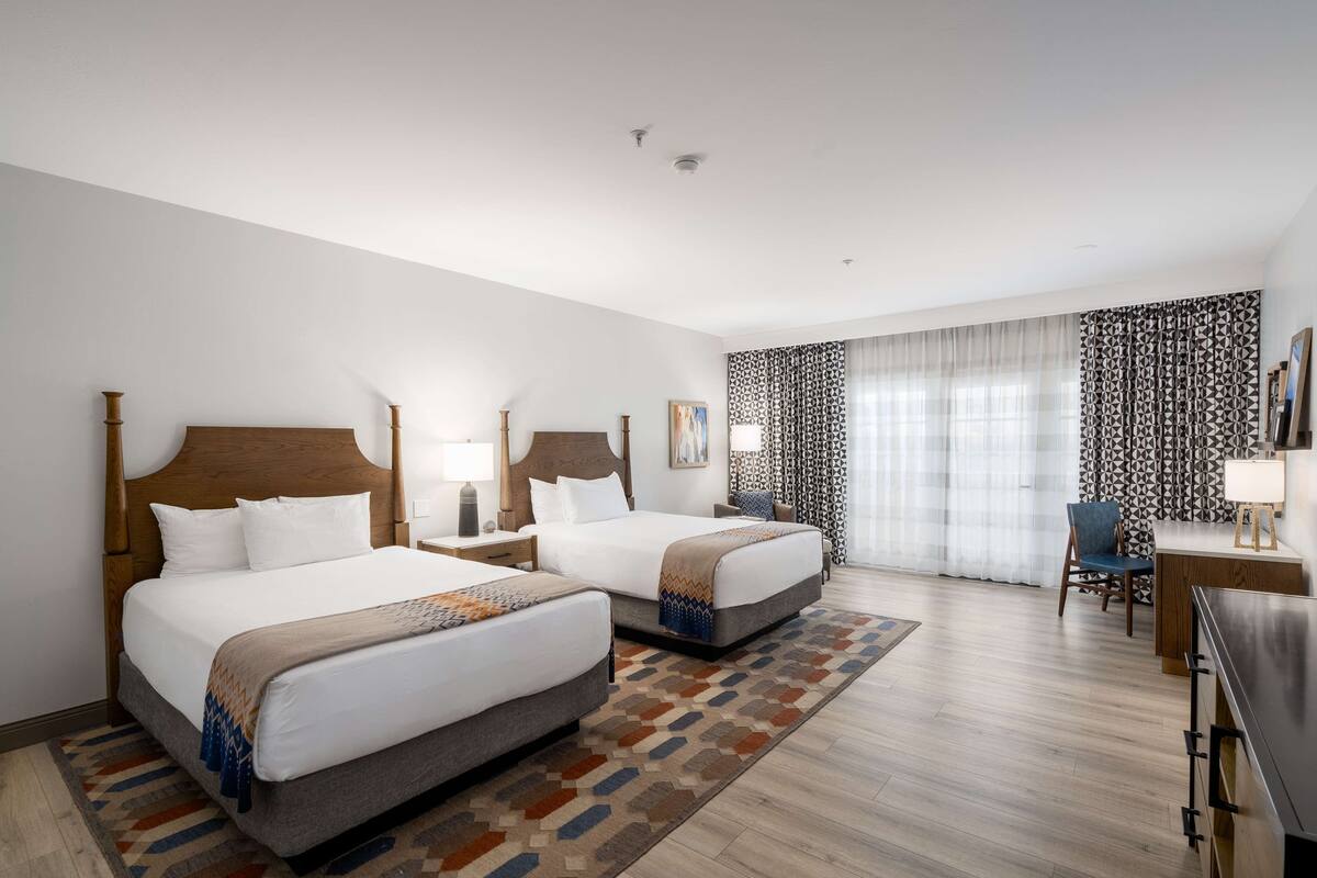 A hotel room with two beds, a desk, a chair, and a TV.