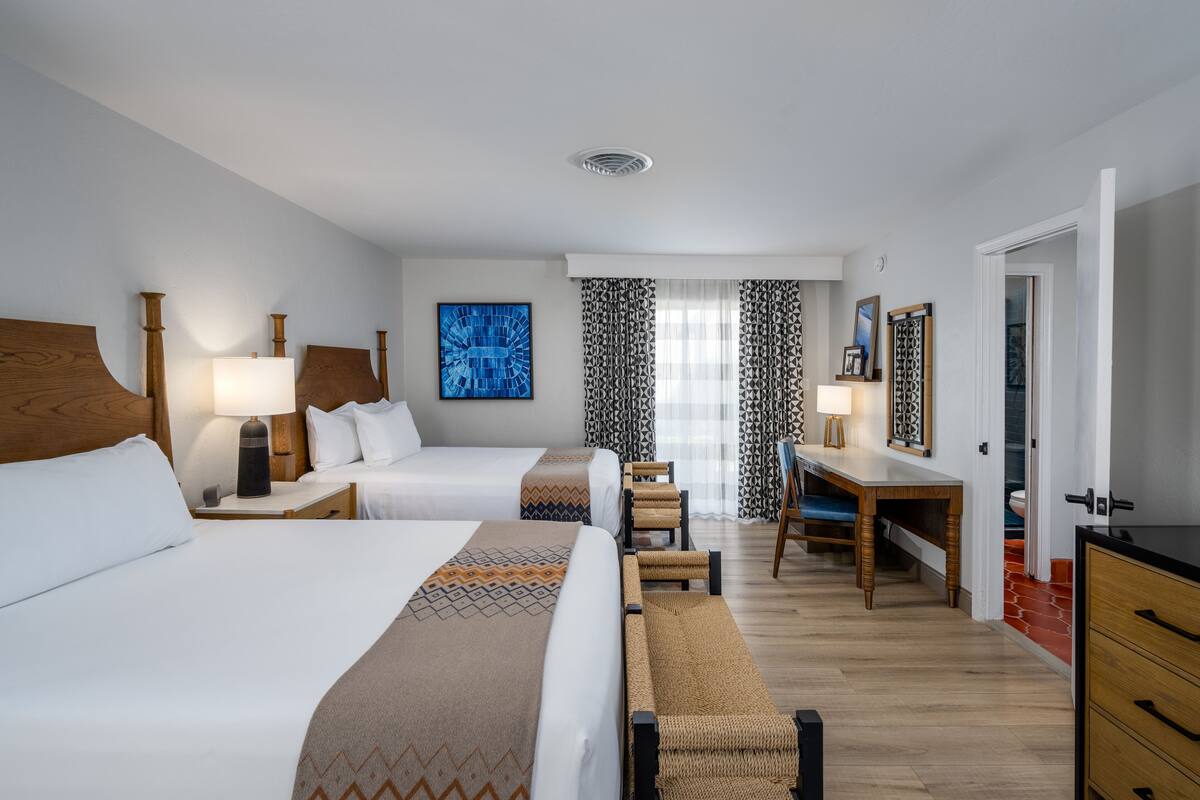 A hotel room with two beds, a desk, a chair, and a wardrobe.