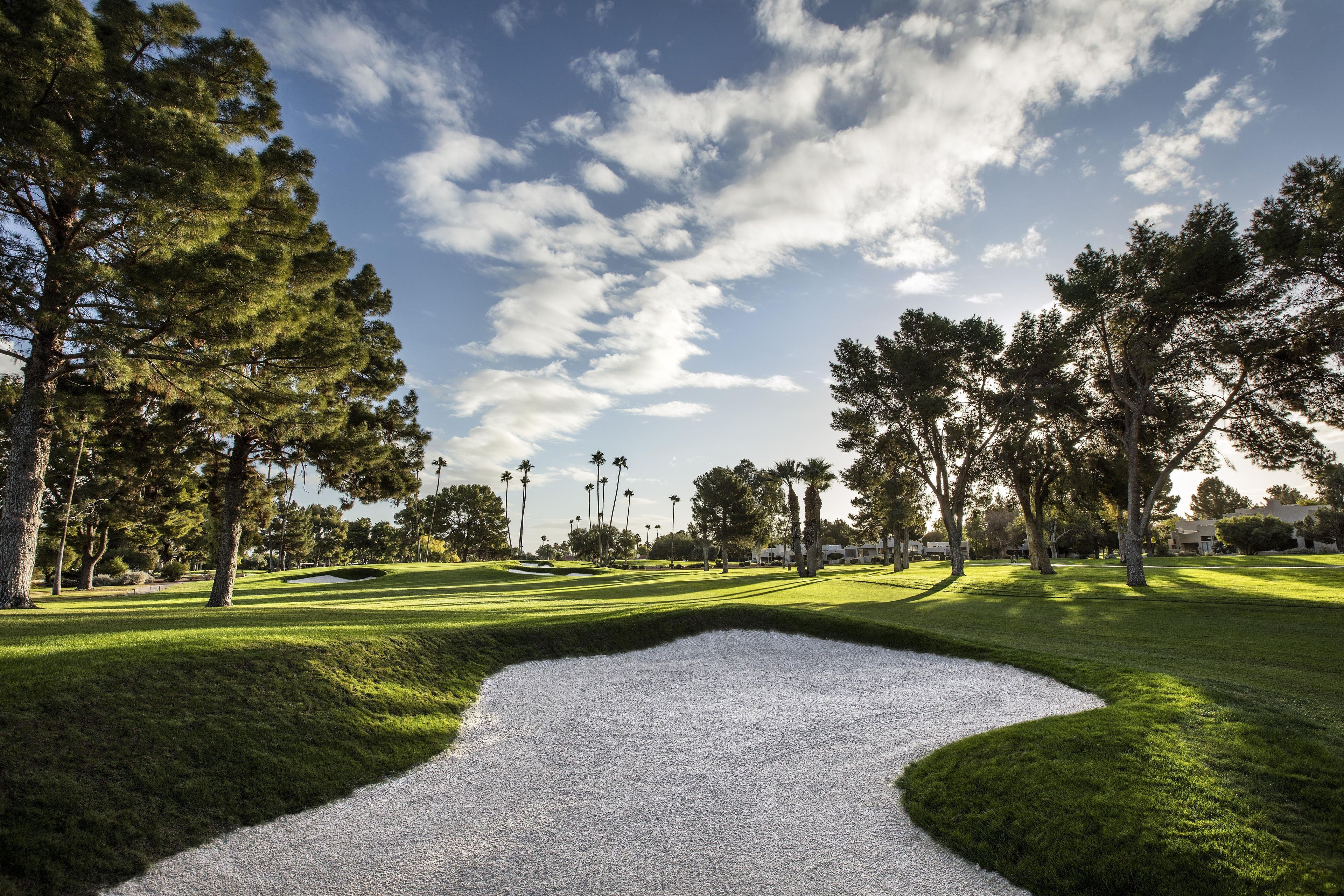A golf course with a putting green, sand bunkers, and a clear sky.