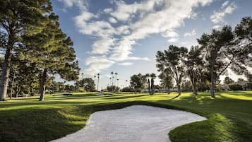 A golf course with a putting green, sand bunkers, and a clear sky.