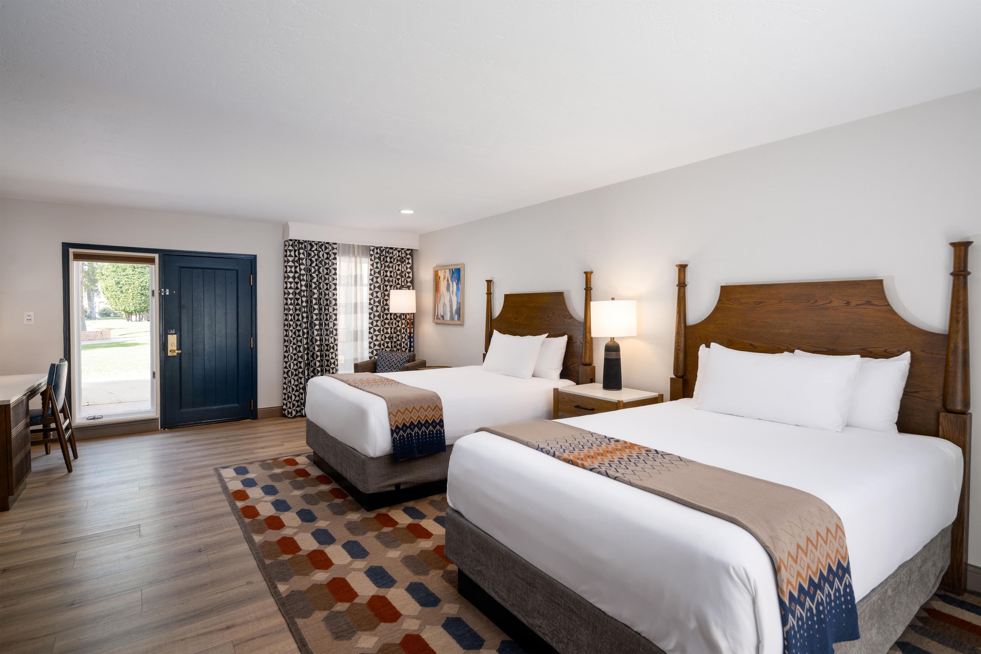 Quarto de hotel com duas camas, uma escrivaninha e porta para uma varanda.