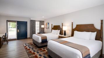 Quarto de hotel com duas camas, uma escrivaninha e porta para uma varanda.