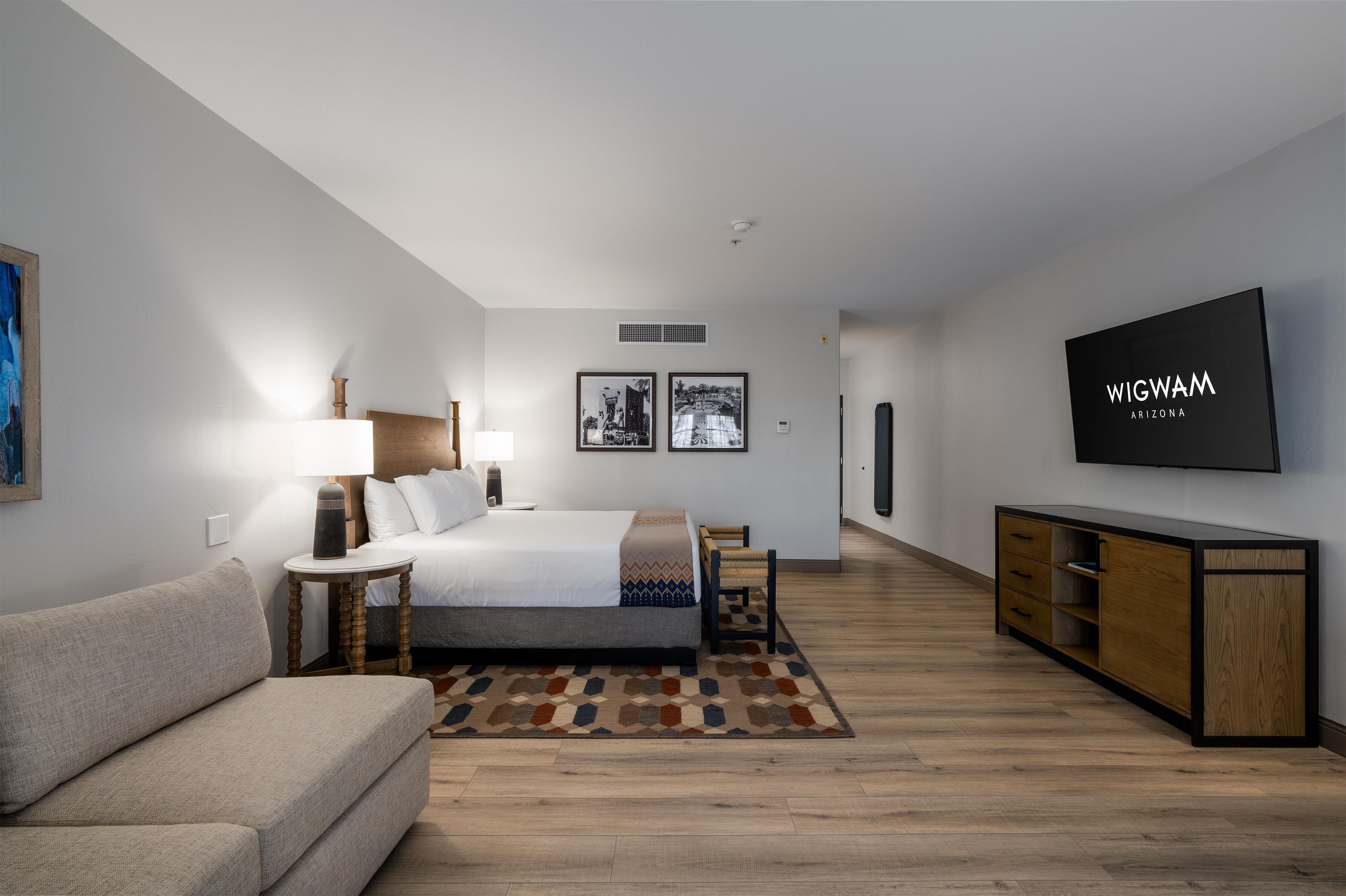 A modern hotel room with a bed, a TV, a sofa, and a desk.