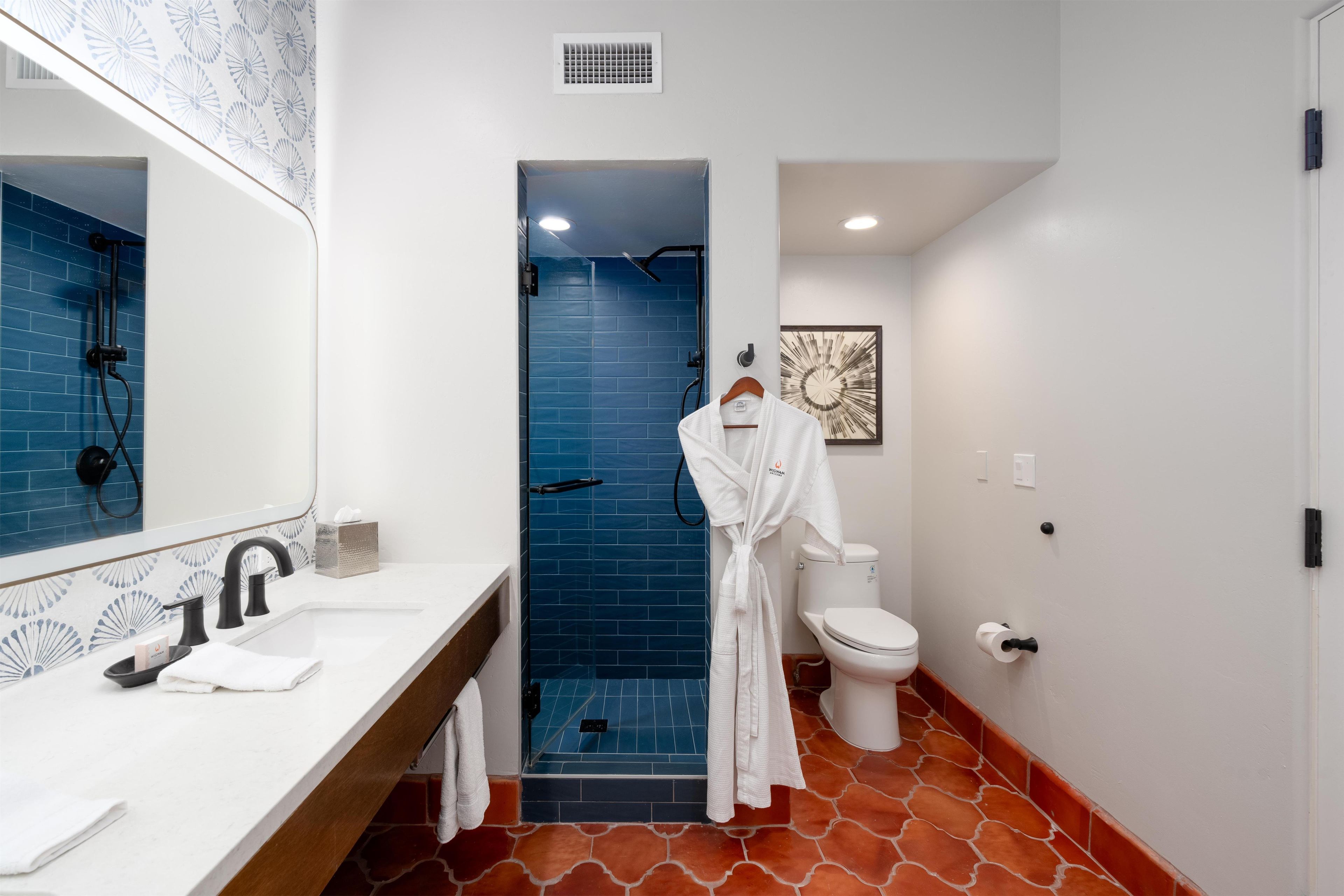 A bathroom with a white sink, a mirror, a towel, a white toilet, and a blue shower enclosure.